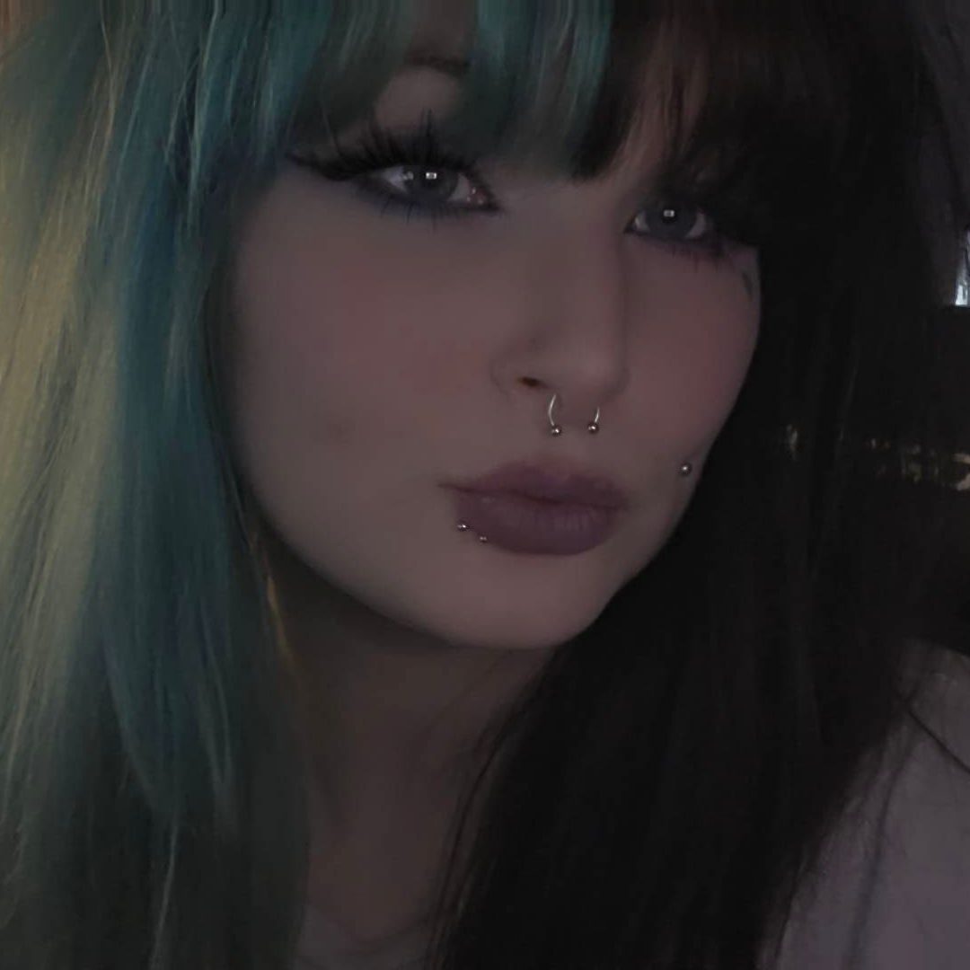 Young woman with blue-tinted hair and a septum piercing, posing closely to the camera.